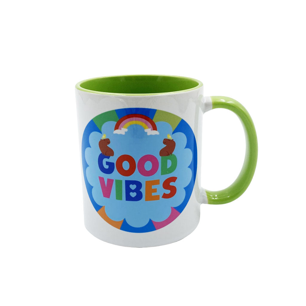 A white ceramic mug with a bright green handle and interior, featuring a colorful 'GOOD VIBES' graphic on the front with a rainbow and blue cloud design.