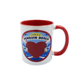 A white ceramic mug with a red interior and red handle, featuring a circular 'Life's a Penguin Beach' graphic on the front.